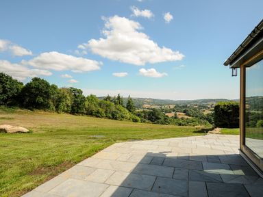 A paved patio with grass and trees overlooking hills at Sandsgate Lodge in Spinster's Rock near Chagford