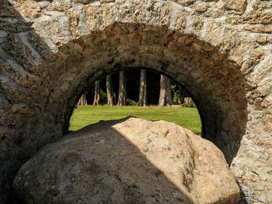 A large rock beneath a stone arch with grass and tree trunks visible in the background at Sandsgate Lodge Spinster's Rock near Chagford