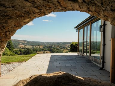 A patio with glass doors opening to a view of rolling hills framed by a stone arch at Sandsgate Lodge Spinster's Rock near Chagford