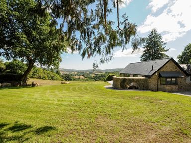 A stone house with a slate roof on a green lawn with trees and hills in the background at Sandsgate Lodge Spinster's Rock near Chagford