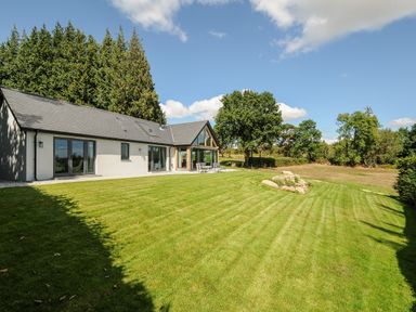 A lawn and patio outside a house with large windows and trees at Sandsgate Lodge Spinster's Rock near Chagford