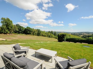 A patio with outdoor chairs and a table overlooking a grassy landscape at Sandsgate Lodge in Spinster's Rock near Chagford