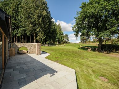 A stone patio next to a grassy yard with trees and a stone wall at Sandsgate Lodge Spinster's Rock near Chagford