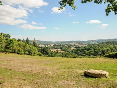 A grassy field with a large rock and trees overlooking rolling hills and a partly cloudy sky at Sandsgate Lodge Spinster's Rock near Chagford