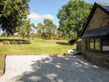 A gravel driveway and stone wall beside a stone house with a lawn and trees at Sandsgate Lodge Spinster's Rock near Chagford