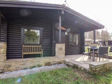 A patio area with a wooden bench and an outdoor dining table with chairs at Alwinton Lodge in Longframlington