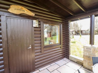 A log cabin entrance with a wooden door and window at Alwinton Lodge in Longframlington