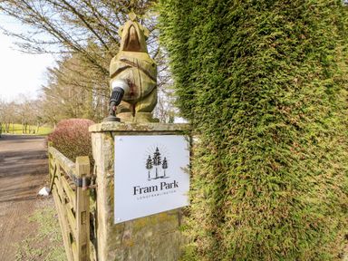 A wooden gate and stone pillar with a sign reading Fram Park Longframlington next to a trimmed hedge