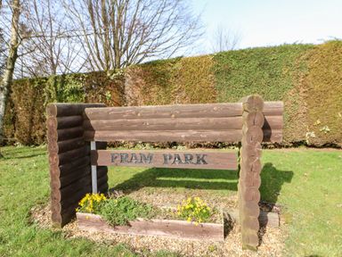 A wooden sign with the text Fram Park surrounded by grass and flowers