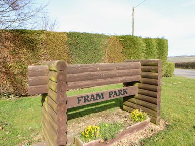 A wooden sign reading Fram Park with yellow flowers and trimmed hedges in the background at Alwinton Lodge in Longframlington