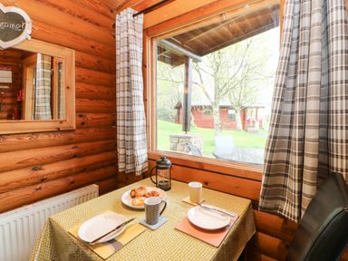 A dining table set for two with plates and mugs by a window in a wooden cabin at Alwinton Lodge in Longframlington