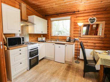 A kitchen with white cabinets a stove microwave and a dining table at Alwinton Lodge in Longframlington