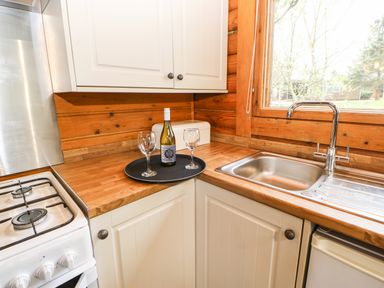 A kitchen corner with a gas stove sink wooden countertops a bottle of wine and two wine glasses on a tray at Alwinton Lodge in Longframlington