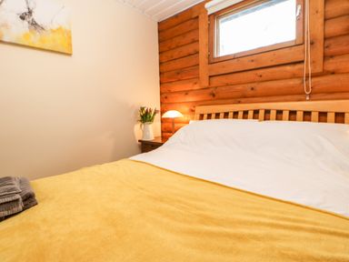 A bedroom with a wooden bed and yellow blanket a nightstand with a lamp and flowers at Alwinton Lodge in Longframlington