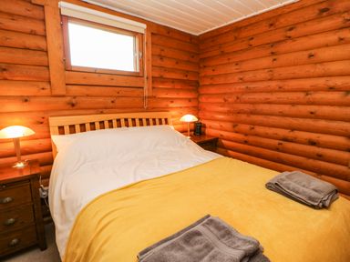 A bedroom with a wooden bed a yellow blanket folded towels on the bed and two bedside tables with lamps at Alwinton Lodge in Longframlington