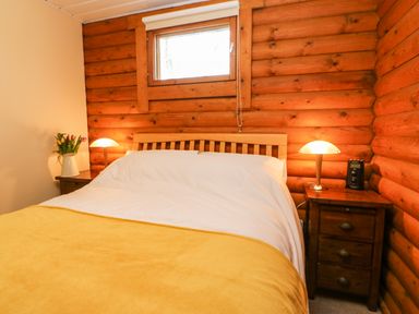 A bedroom with a bed covered in white and yellow bedding between two wooden nightstands with lamps and a small window above the headboard at Alwinton Lodge in Longframlington