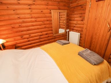 A bedroom with a bed covered in white sheets and a yellow blanket with towels on top in a wooden log cabin at Alwinton Lodge in Longframlington