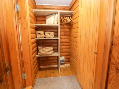A wooden closet with shelves holding baskets and pillows and hangers on a rod at Alwinton Lodge in Longframlington