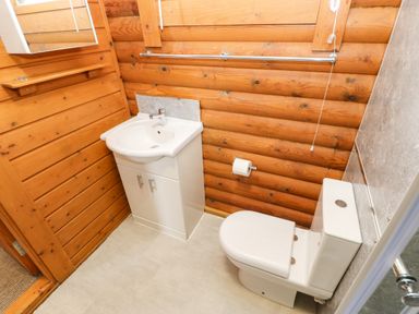 A bathroom with a white toilet and sink against wooden log walls at Alwinton Lodge Longframlington