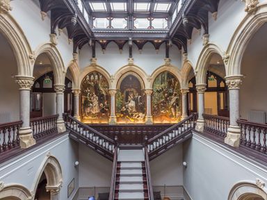 A grand staircase with wooden railings and arched stone columns with paintings on the wall at William Tower Suite Stone Cross Mansion Ulverston