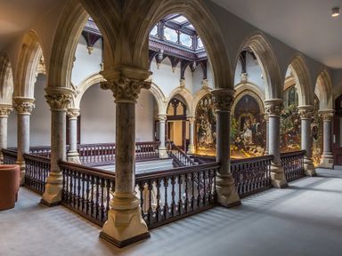 A hallway with arched pillars and wooden railings overlooking a lower floor at William Tower Suite Stone Cross Mansion in Ulverston