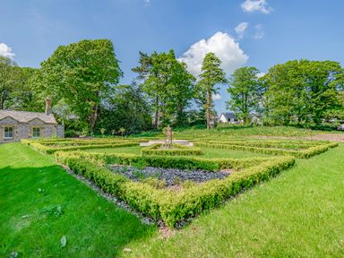 A garden with trimmed hedges and green grass with trees and stone house at William Tower Suite Stone Cross Mansion in Ulverston