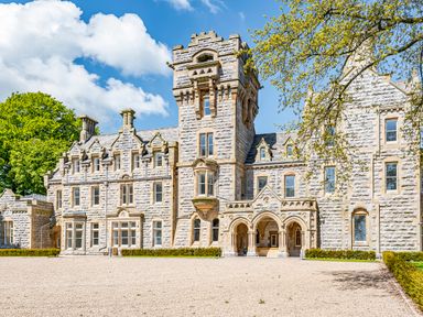 Exterior view of a stone mansion with a central tower and arched entrance surrounded by trees at William Tower Suite Stone Cross Mansion in Ulverston