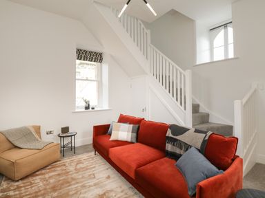A living room with a red sofa a brown armchair and a staircase at William Tower Suite Stone Cross Mansion in Ulverston