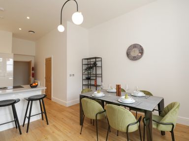 A dining area with six green chairs around a rectangular table set with plates and glasses at William Tower Suite Stone Cross Mansion in Ulverston