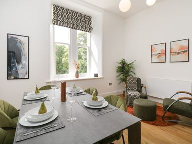 A dining area with a set table and green chairs next to a window and a sitting area with chairs and artwork at William Tower Suite Stone Cross Mansion Ulverston