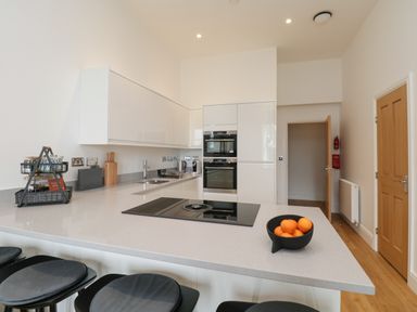 A kitchen with a countertop island with stools and built-in appliances at William Tower Suite Stone Cross Mansion Ulverston