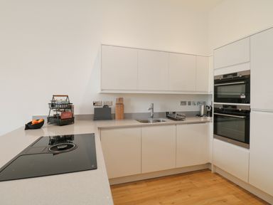 A kitchen with white cabinets, a stovetop, double oven, sink, and countertop appliances at William Tower Suite Stone Cross Mansion in Ulverston