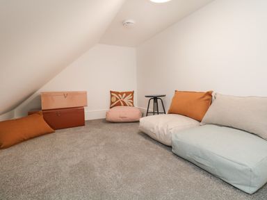 A small room with slanted ceiling containing floor cushions, pillows, two stacked storage boxes and a small black stool at William Tower Suite Stone Cross Mansion in Ulverston