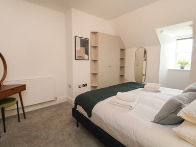 A bedroom with a bed with folded towels bedside table with a round mirror wall mirror wardrobe and a window at William Tower Suite Stone Cross Mansion in Ulverston