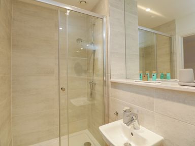 A bathroom with a glass shower enclosure and a white sink with a mirror above at William Tower Suite Stone Cross Mansion in Ulverston