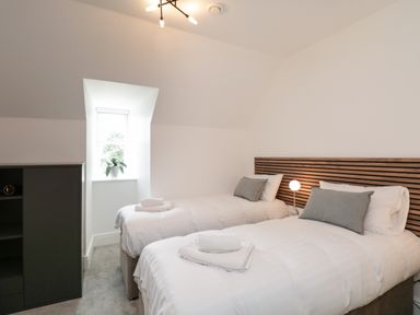 A bedroom with two single beds a wooden headboard a small window with a plant and a black cabinet at William Tower Suite Stone Cross Mansion Ulverston