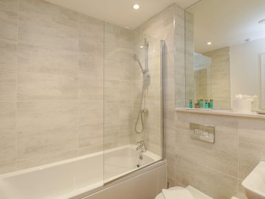 A bathroom with a bathtub shower combination and toiletries on a shelf at William Tower Suite Stone Cross Mansion in Ulverston