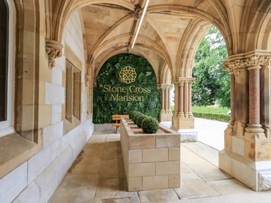 A stone archway corridor with decorative columns and a planter with bushes at Stone Cross Mansion
