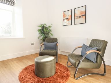 A sitting area with two chairs a round ottoman on a circular rug and two framed pictures on the wall at William Tower Suite Stone Cross Mansion in Ulverston
