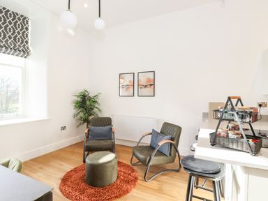 A sitting area with two chairs a round rug and a small round ottoman beside a kitchen counter with two bar stools at William Tower Suite Stone Cross Mansion in Ulverston