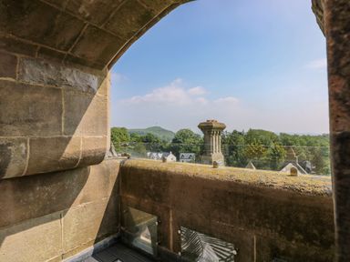A stone balcony with glass railing overlooking trees houses and a hill at William Tower Suite Stone Cross Mansion in Ulverston
