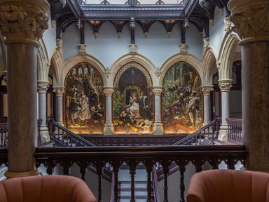 A hall with arches and large paintings above a staircase with chairs in the foreground at The Elizabeth Suite Stone Cross Mansion Ulverston