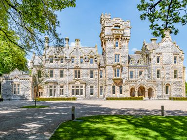 A stone mansion with multiple windows towers and an arched entrance surrounded by trees and a lawn at The Elizabeth Suite Stone Cross Mansion in Ulverston