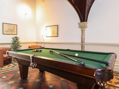 A room with a pool table with cues and balls two armchairs a plant framed pictures and a decorative column at The Elizabeth Suite Stone Cross Mansion in Ulverston