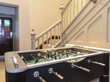 A foosball table next to a staircase with white railings and beige walls at The Elizabeth Suite Stone Cross Mansion in Ulverston