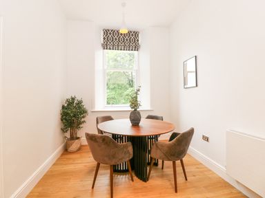 A dining area with a round table and four chairs near a window with a potted plant in the corner at The Elizabeth Suite Stone Cross Mansion Ulverston