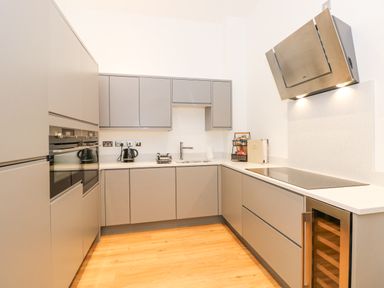 A kitchen with grey cabinets wooden floor an oven sink stovetop and wine cooler at The Elizabeth Suite Stone Cross Mansion Ulverston