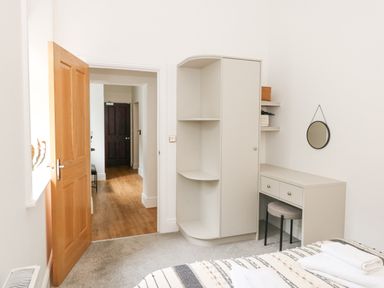 A bedroom with an open wooden door a white wardrobe a dressing table with a round mirror and a bed at The Elizabeth Suite Stone Cross Mansion Ulverston