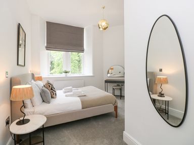 A bedroom with a bed bedside tables lamps a wall mirror and a dressing table at The Elizabeth Suite Stone Cross Mansion in Ulverston