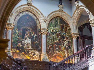A staircase with wood railing and two large paintings on arched wall panels at The Alfred Suite Stone Cross Mansion in Ulverston